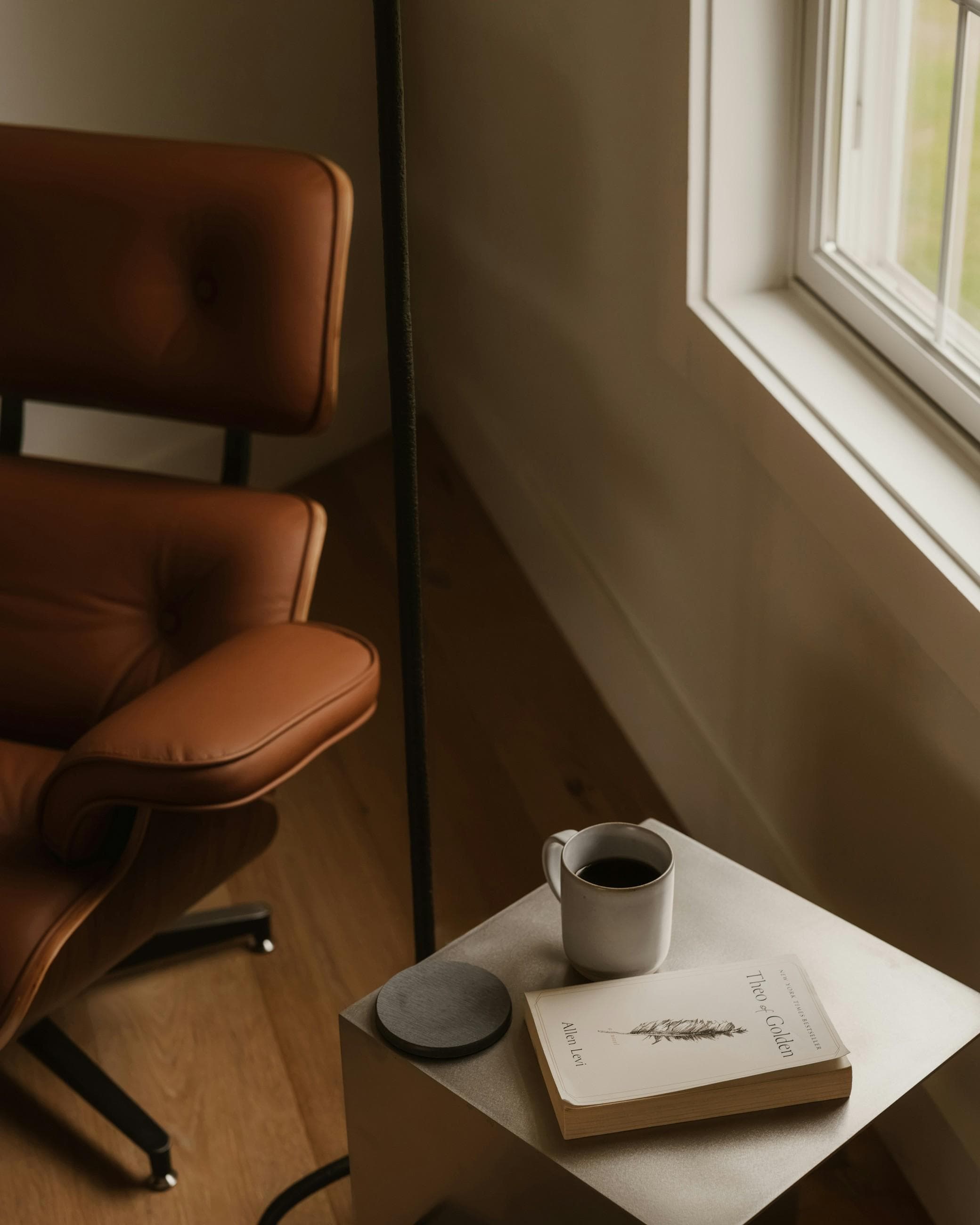 Un fauteuil en cuir près d’une fenêtre et, sur la table d’appoint, un livre et une tasse