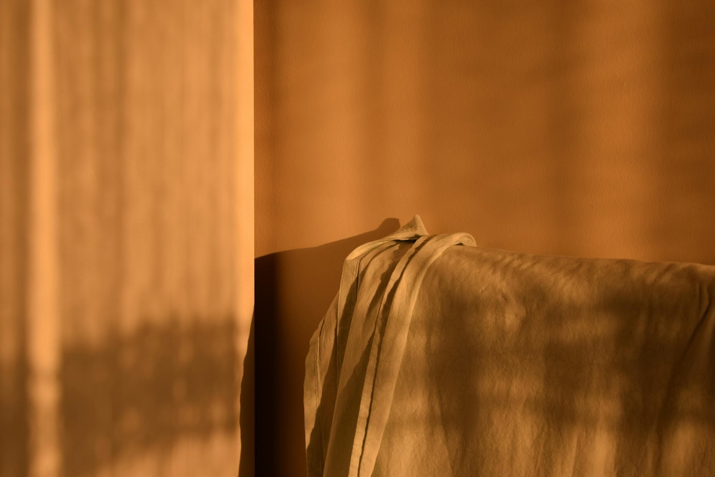 Une lumière chaude à travers un voilage, et un plaid de lin jeté sur le dossier d’un siège